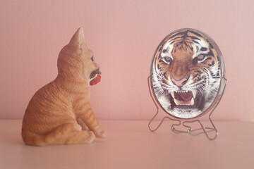 Kitten looks in the mirror and sees himself reflected like a tiger. Self-confidence concept. Business or personal growth.