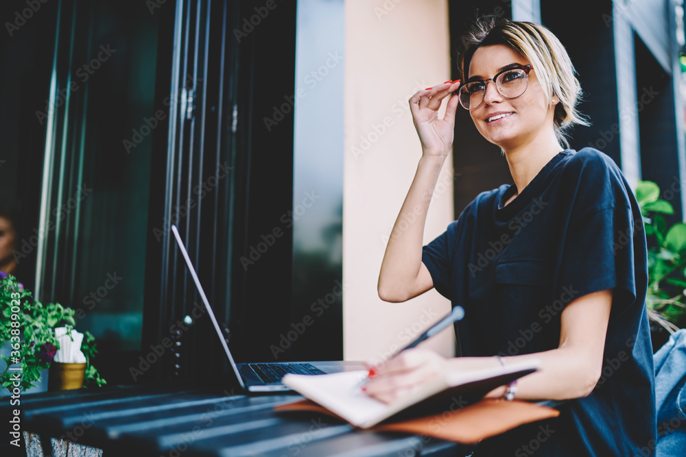 Poster smiling fashionable hipster woman distracted from work on modern laptop computer, female programmer 
