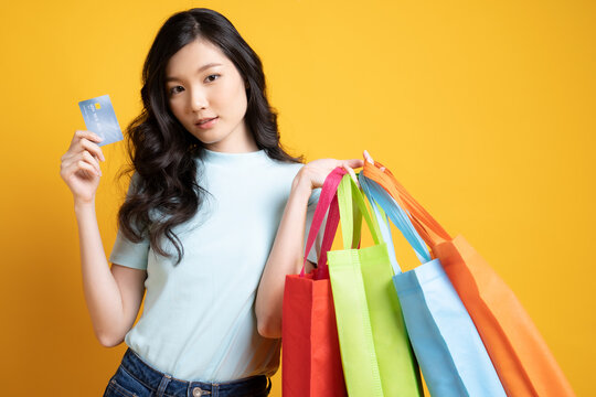 young Asian woman with shopping bags and credit card image isolated on yellow background