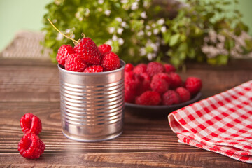 Fresh ripe organic raspberry in tin can and plate on rustic wooden table.