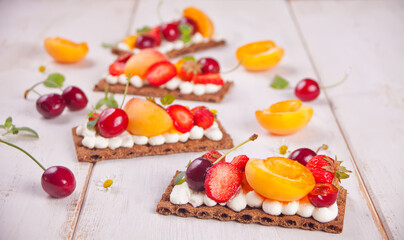 Crisp fitness health bread with creme cheese, fruit and berries on the white wooden background.