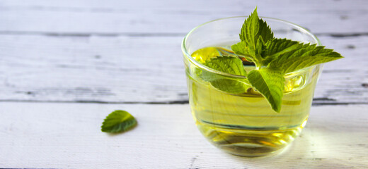 Fresh mint tea concept on a wooden background. Mint tea in a transparent cup and one mint leaf on the table. Banner.