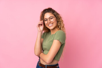 Young blonde woman with curly hair isolated on pink background with glasses and happy