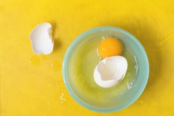 Raw egg white and wgg yolk in a bowl on a yellow tray, above vantage point photography, close up