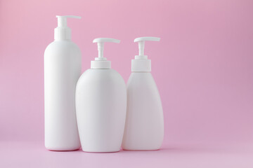 White plastic bottles on a pink background, a set of cosmetic containers with a dispenser. Copy space, empty place for text. Toiletries, pump lotion. Moisturizing cream for body and face.