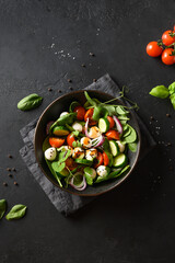 Salad with spinach, summer vegetables and Mozzarella on black background. Top view. Vertical