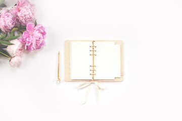 Female diary, golden pen and pink peonies on a white background. Copy space.