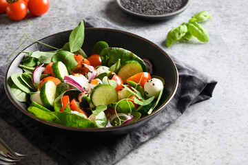 Salad with spinach, cherry tomatoes, onion and Mozzarella on grey stone background. Close up.