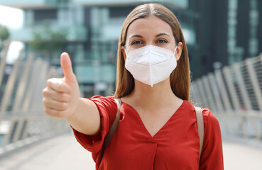 COVID-19 Optimistic business woman wearing protective mask KN95 FFP2  showing thumbs up in modern...