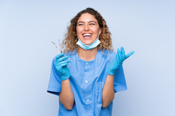 Young blonde woman dentist holding tools isolated on blue background laughing