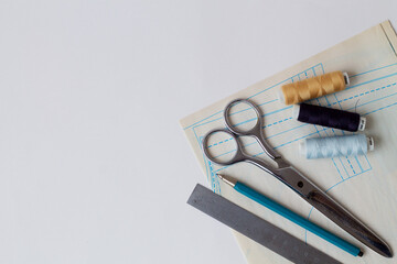 needlework. sewing thread, pencils, ruler, scissors and patterns on a white table of a fashion designer. top view. copy space. offices tools on white background