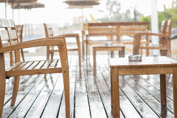 Focus on the chair and the table at the beach bar. It is currently raining heavily and there are no guests.