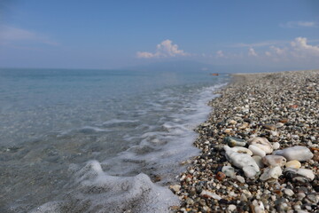 A beautiful view of the sea pebble, wet from the rising waves, sea foam in the foreground, sunshine on the surface of the pebble, blue sky and calm sea on a summer sunny day, , italy, calabria