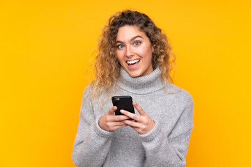 Fototapeta premium Young blonde woman with curly hair wearing a turtleneck sweater isolated on yellow background surprised and sending a message