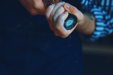 A chef in a blue apron holds a glass salt shaker with peas of various peppers inside and pepper the...