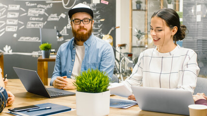 Shot of Two Young Developers Have Daily Meeting, Where Their Discuss Ongoing Project, Using Laptop, Consulting Various Data. Stylish People in Trendy Office Space.