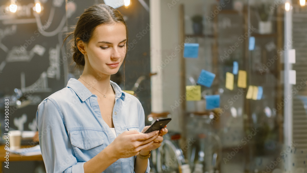 Aufkleber charming young woman uses smartphone while smiling and standing in the busy creative office with sty