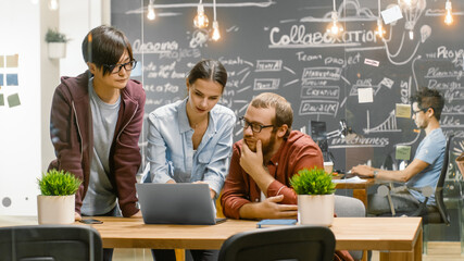 Three Creative People Have Active Discussion About Ongoing Project While Using Laptop. Stylish...