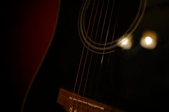 A deliberately underexposed, dark image of a black guitar. The details of the strings and smooth shape of the guitar are clearly visible. A light red glow in the background sets a romantic mood.