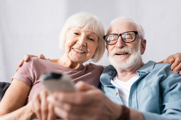 Selective focus of elderly couple smiling and holding remote controller of air conditioner at home