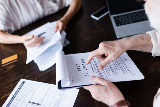 Cropped view of senior man pointing at paper with debt collection lettering near gadgets and wife at home