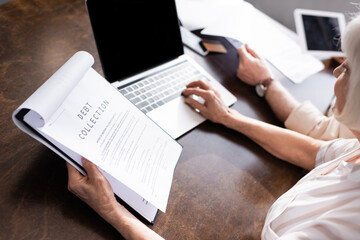 Selective focus of woman using laptop and holding papers with debt collection lettering near man at table