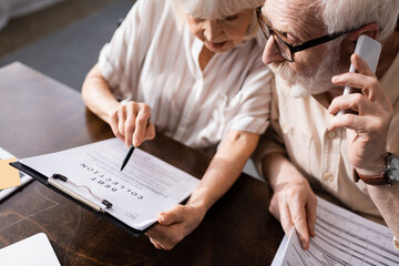 High angle view of senior man talking on smartphone near wife pointing at document with debt collection lettering