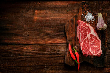 Raw Flat Iron beef steak on a wooden Board with red pepper, top view and copy space