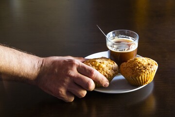 Closeup shot of male hand taking the muffin from a plate with a cup of coffee and another muffin