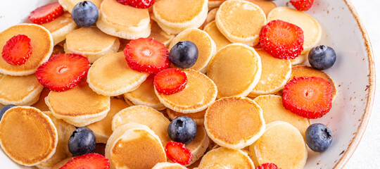Fototapeta na wymiar Tiny pancakes with strawberries and blueberries for breakfast.