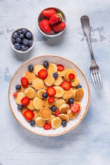 Tiny pancakes with strawberries and blueberries for breakfast.