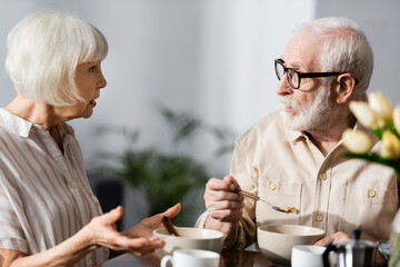 Selective focus of elderly couple talking during breakfast at home