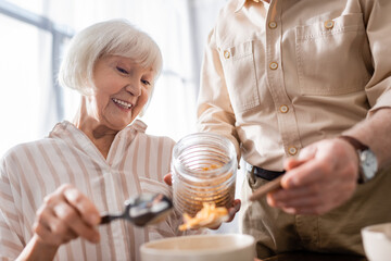 Selective focus of senor man pouring cereals in bowl near smiling wife in kitchen