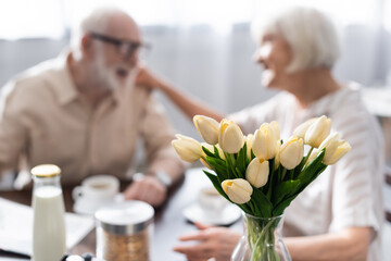 Selective focus of tulips in vase and senior couple sitting at table during breakfast
