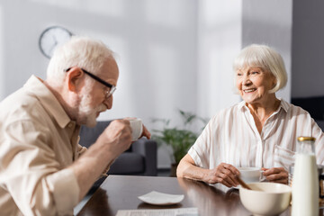 Selective focus of smiling senior woman looking at husband drinking coffee at home