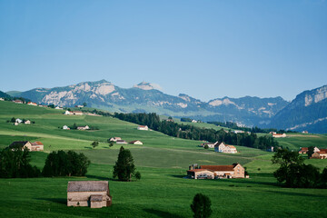 Fototapeta na wymiar Beautiful summer landscape with houses on green field, Swiss Alps Mountains.