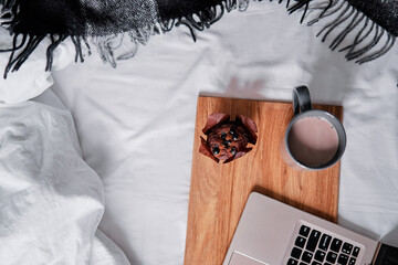 Breakfast in bed: a wooden tray with muffin and cup of cocoa and laptop computer.