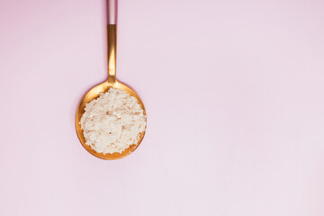 Collagen powder in a spoon on pink background