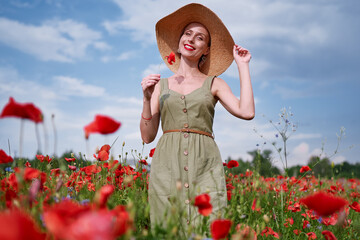 Summertime. Young woman in dress walking on red poppy field.