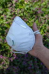 Close up white anti virus filter mask in hand, side view. Green floral background.