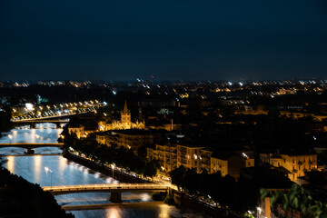 Fototapeta na wymiar Night photo with moon in sky view along Adige river with view of Ponte Nuovo and Ponte Navi with church of saint Fermo Maggiore, city of Verona, Italy.