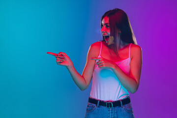 Pointing, choosing, laughting. Caucasian young woman's portrait on gradient background in neon light. Beautiful female model. Concept of human emotions, facial expression, sales, ad. Copyspace.