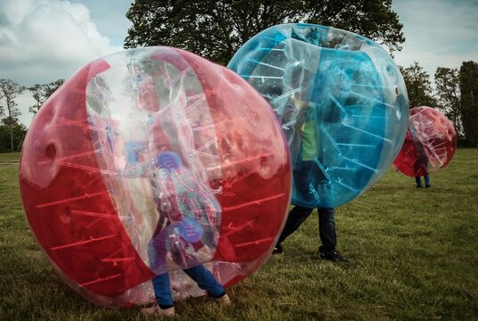 Boys And Girl Playing Bubble Soccer On Grassy Field
