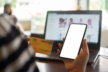 Mockup blank white screen mobile phone for online shopping in internet concept. Woman using credit card and blank smartphone for shopping clothes online.