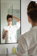 Obraz premium Kobieta wiązała włosy, patrząc w lustro