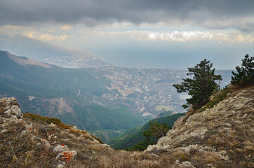 View from the mountain edge to the Yalta city in Wuchang-Su Valley on the Black Sea coast in south Crimea. Dry grass and stones in the foreground. Forest on the slope. City on the shore. Cloudy sky.
