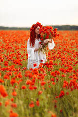 Beautiful redhead smiling woman in wreath with bouquet of poppies on green field