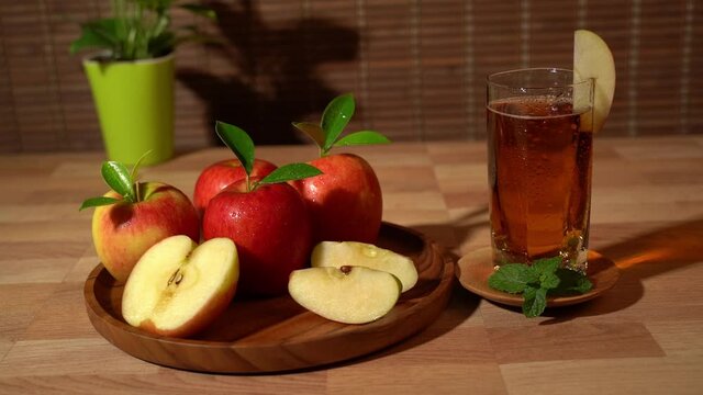 Glass of apple juice and a red apple on the wooden tray.
