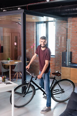 Fototapeta na wymiar cheerful businessman standing with bicycle in modern office