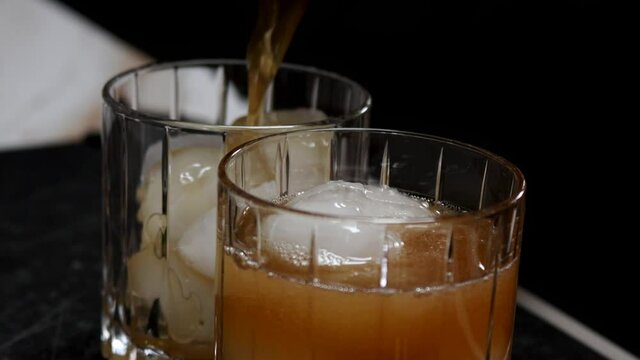Pouring two mixed drinks over ice in slow motion